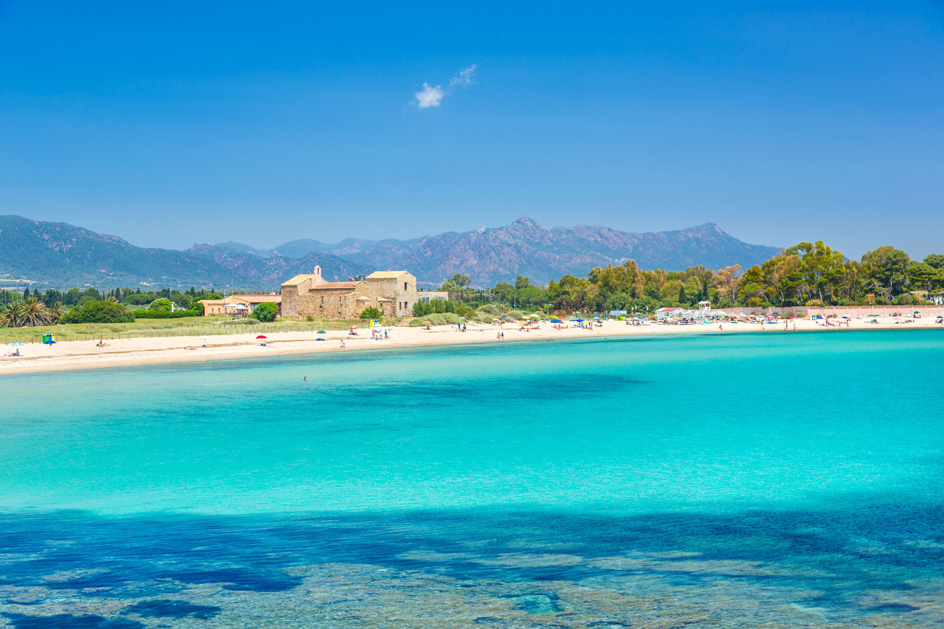 Spiaggia di Nora a Pula con mare cristallino e la chiesetta di Sant'Efisio sullo sfondo.