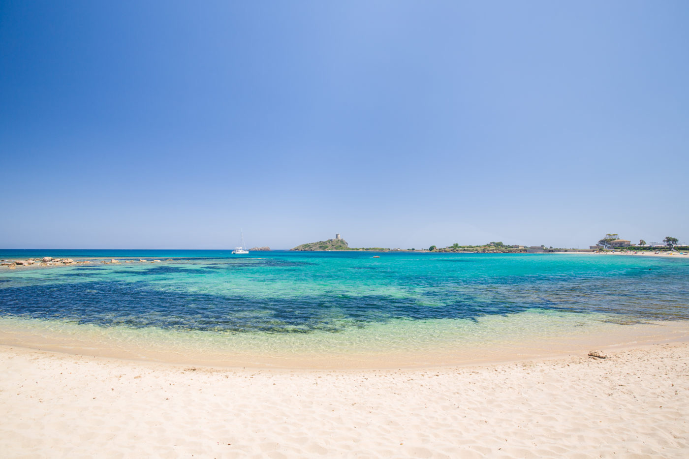 Panorama della Spiaggia dei Fichi a Pula con acque color smeraldo e sabbia finissima.